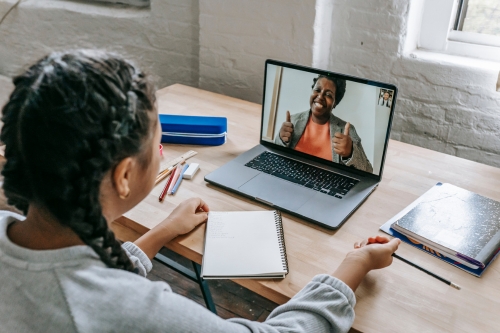 girl sat at desk speaking to tutor on video call on laptop